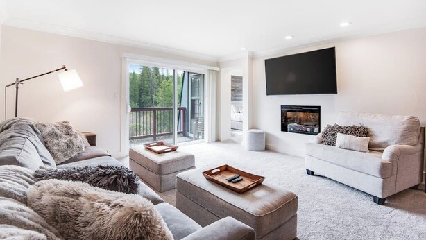 Een moderne woonkamer met een bank, een voetenbankje en een flatscreen televisie aan de muur.