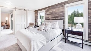 Een slaapkamer met een groot bed, een nachtkastje, een raam met uitzicht en een deur naar een andere kamer.