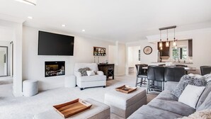 Een moderne woonkamer met een flatscreen televisie, een open haard, een eethoek met barkrukken en een keuken met hanglampen.