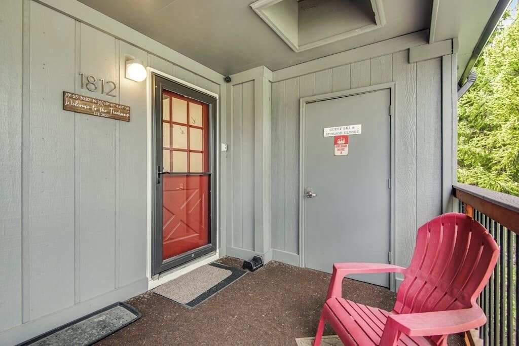 A building entrance with a red door, a number plaque, a guest notice, and a red chair outside.