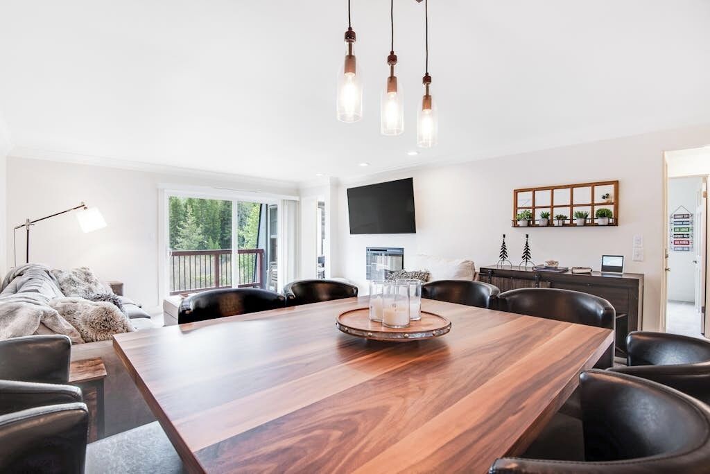 Een moderne eethoek met een houten tafel, zwarte lederen stoelen en hanglampen.