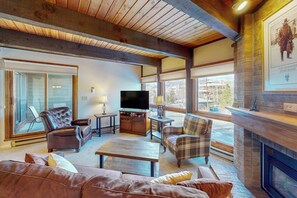 Ein Wohnzimmer mit Kamin, Ledersofas, einem Fernseher und einem großen Fenster.