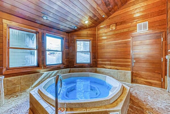 Ein Holzblockhaus-Interieur mit Whirlpool, großen Fenstern und einer Tür.