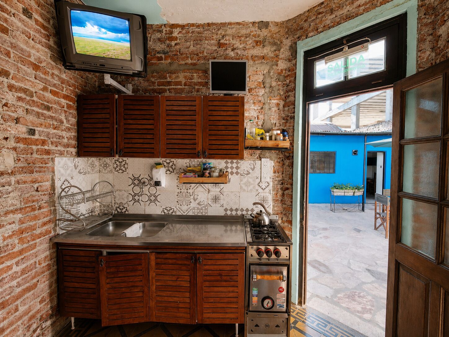 Une cuisine avec un mur en briques, des armoires en bois, un pare-feu en carreaux, une cuisinière et un téléviseur fixé au-dessus de l’évier.