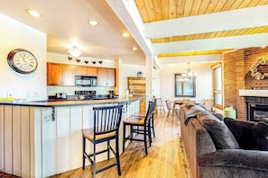 Eine moderne Küche mit Holzausstattung, einer zentralen Kochinsel mit Barhocker, einem Essbereich mit einer Chandelieber und einem Wohnzimmer mit Kamin.
