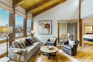 Ein geräumiges Wohnzimmer mit Sofa, Sesseln, einem Couchtisch und einem großen Fenster mit Blick nach draußen.