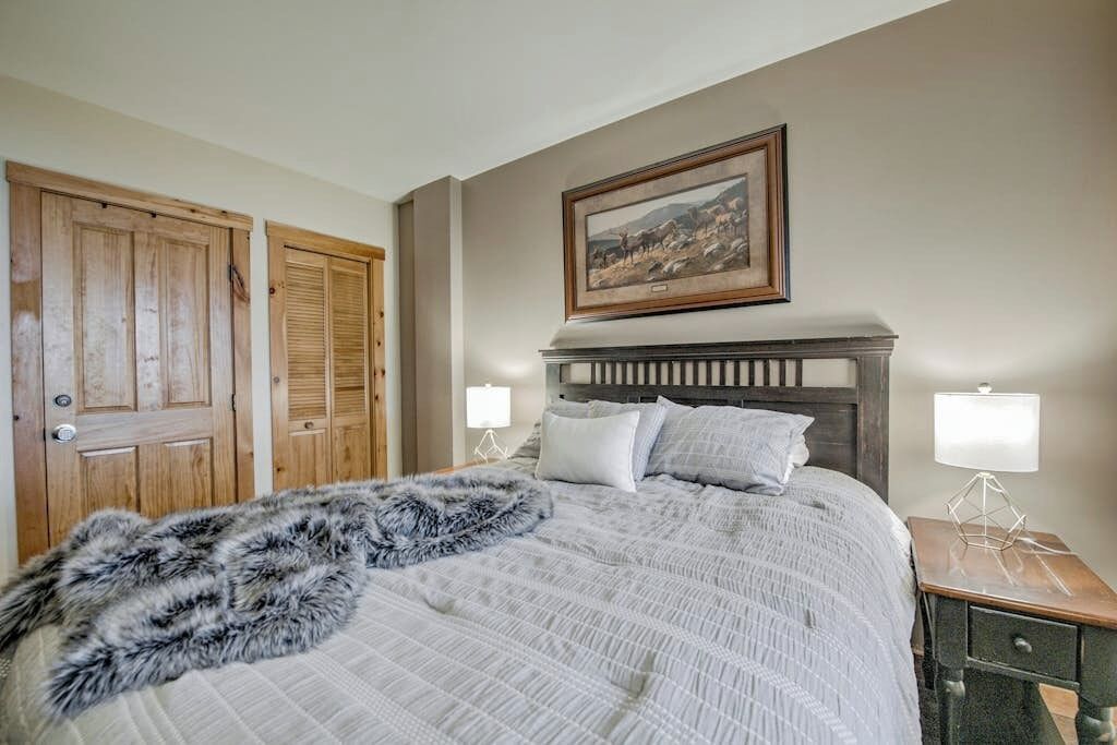 A bedroom with a bed, two bedside lamps, a framed picture on the wall, and wooden doors.