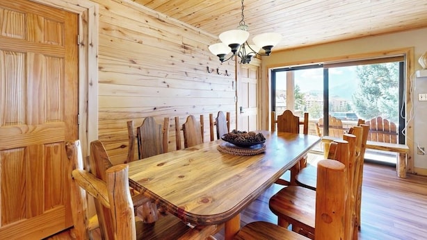 A wooden interior with a dining table, chairs, a chandelier, and a large window. - Charming condo with mountain views, washer/dryer, & shared hot tub (Crested Butte)