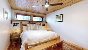 A bedroom with a wooden ceiling, a bed with white bedding, a wooden bench, a nightstand, and a ceiling fan. - Charming condo with mountain views, washer/dryer, & shared hot tub (Crested Butte)