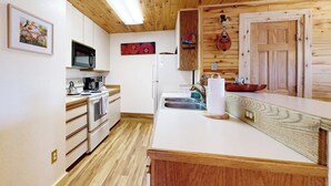 A kitchen with wooden ceiling, white cabinets, a microwave, a stove, a sink, and a wooden door. - Charming condo with mountain views, washer/dryer, & shared hot tub (Crested Butte)