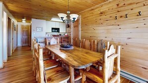 A wooden interior with a dining table and chairs, a kitchen in the background, and a ceiling with wooden beams. - Charming condo with mountain views, washer/dryer, & shared hot tub (Crested Butte)