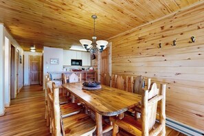 Ein Holzinnenraum mit Esstisch und Stühlen, eine Küche im Hintergrund und eine Decke mit Holzbalken.