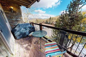 A balcony with a glass table and chairs, a stone wall, and a view of trees and mountains. - Inviting Snowmass condo short walk from activities with balcony (Snowmass Village)