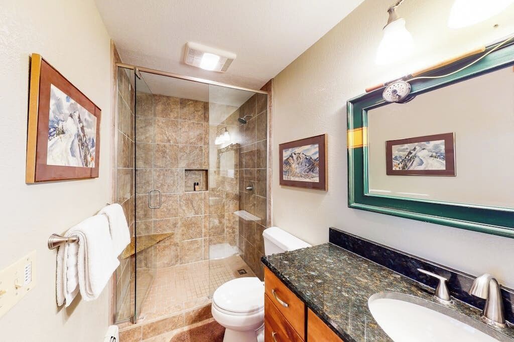 A bathroom with a glass-enclosed shower, a toilet, a sink, and framed pictures on the walls.
