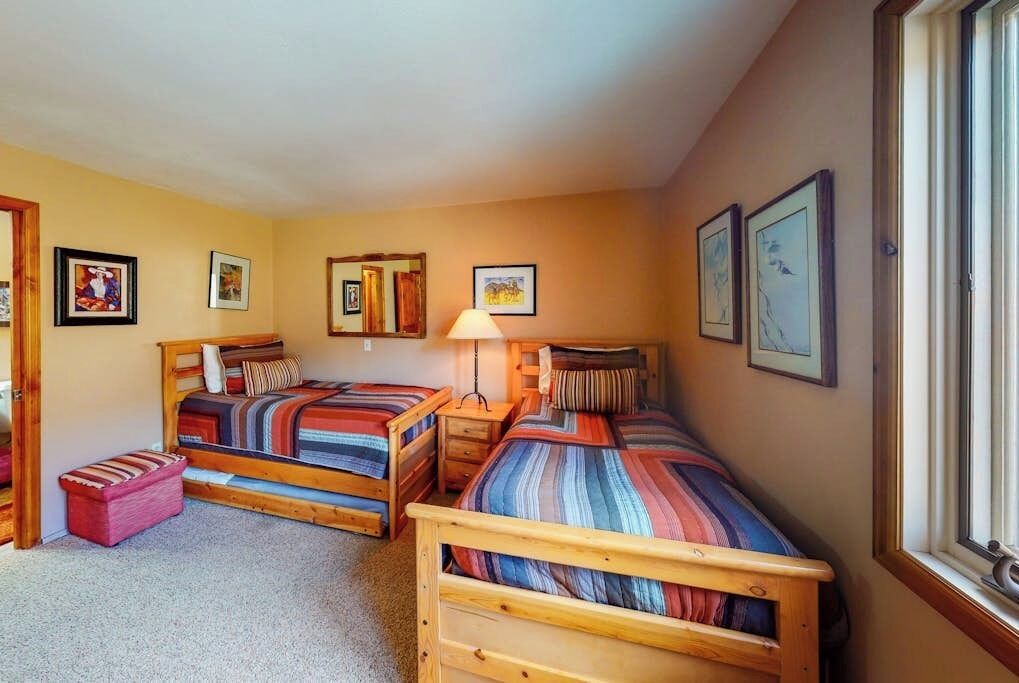 Un dormitorio con dos camas de madera, un taburete pequeño y cuadros enmarcados en las paredes.