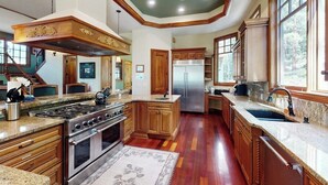 A spacious kitchen with wooden cabinets, a stainless steel refrigerator, and a large island. - Luxury mountain estate w/ private hot tub, home theater, two W/Ds, & spa (Keystone)
