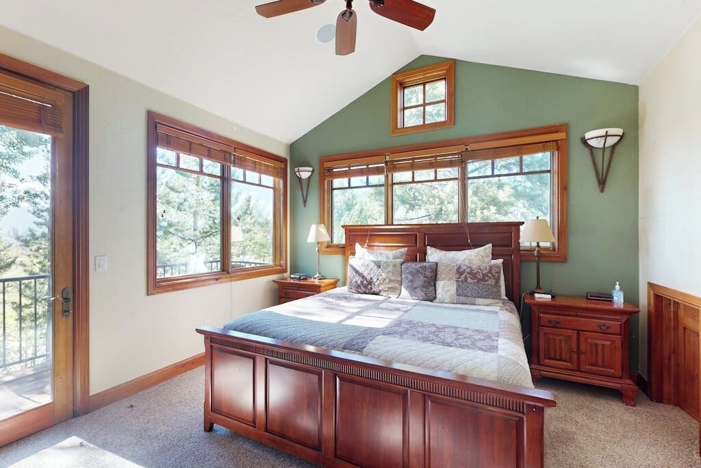 Ein Schlafzimmer mit einem großen Bett, einem Holzkopfende, zwei Nachttischen, einem Beistelltisch, einem Deckenventilator und großen Fenstern.