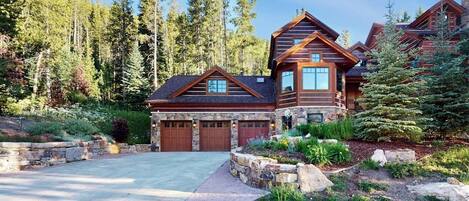 A large log cabin with multiple garage doors, surrounded by a stone retaining wall and a landscaped garden.