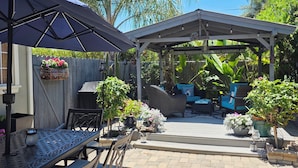 Un patio cubierto con mobiliario exterior, una pérgola y plantas en macetas.