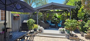 Eine überdachte Terrasse mit Gartenmöbeln, einer Pergola und Blumentöpfen.