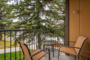 Ein Balkon mit zwei Stühlen und einem kleinen Tisch, mit Blick auf eine Straße und einen großen immergrünen Baum.