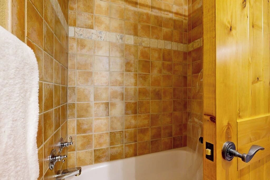 Ein Badezimmer mit Badewanne, einer Holztür und Fliesenwänden.