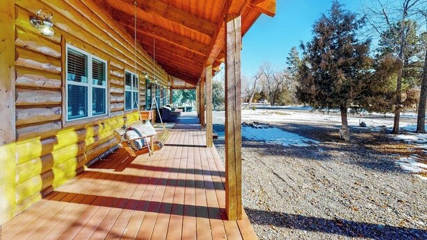 Uma cabana de toras com varanda, área de estar externa e vista para uma paisagem nevada.