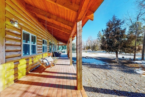 Eine Blockhütte mit Veranda, Sitzgelegenheit im Freien und Blick auf eine verschneite Landschaft.