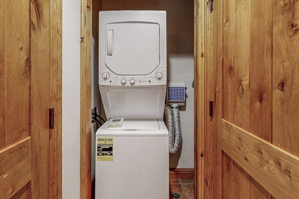 Et vaskerum med vaskemaskine og tørretumbler stablet oven på hinanden, en stikkontakt og en udluftningsslange.