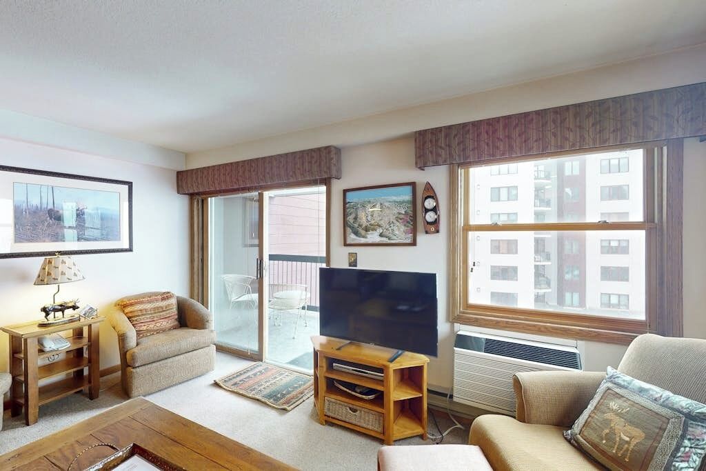 Una sala de estar con televisor, sofá y ventana con vista a edificios.