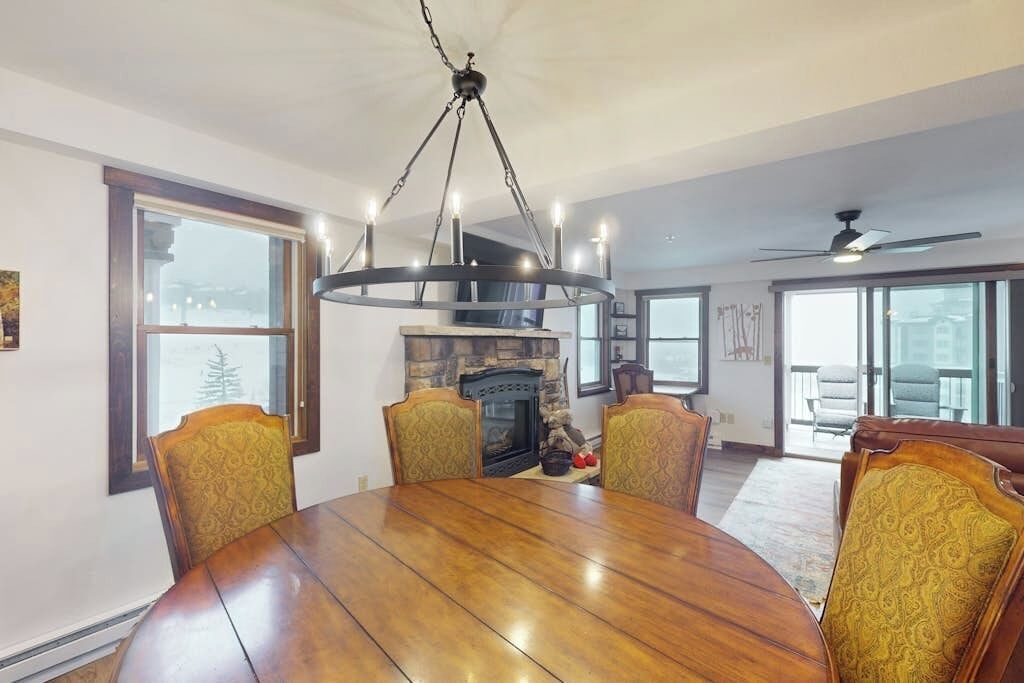 A dining room with a wooden table, four chairs, a fireplace, and a chandelier.