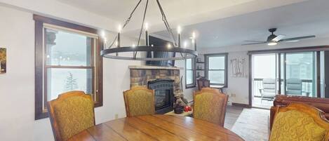 A dining room with a wooden table, four chairs, a fireplace, and a chandelier.