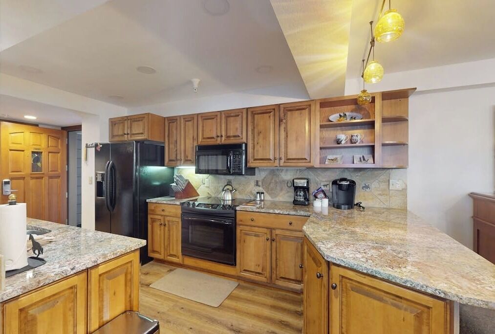 A kitchen with wooden cabinets, granite countertops, a refrigerator, stove, microwave, and a coffee maker.