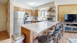 Una cocina moderna con una isla central, taburetes de bar, refrigerador, microondas, horno y televisión.