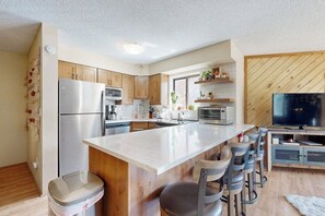 A modern kitchen with a central island, bar stools, a refrigerator, microwave, oven, and a television. - Lovely getaway with, hot tubs & gym - close to lifts & activities (Breckenridge)
