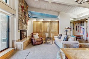 A living room with a stone wall, wooden paneling, a fireplace, leather armchair, and a sofa. - Ski-In/Out Top-Floor Condo w/Free WiFi, Fireplace, and Shared W/D, Hot Tub, Pool (Steamboat Springs)