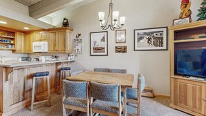 Une cuisine avec des meubles en bois, un four à micro-ondes, une table à manger avec des chaises, un lustre et des tableaux encadrés accrochés au mur.