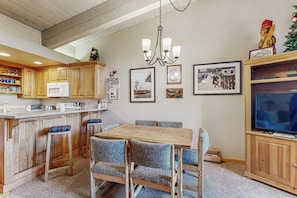 A kitchen with wooden cabinets, a microwave, a dining table with chairs, a chandelier, and framed pictures on the wall. - Ski-In/Out Top-Floor Condo w/Free WiFi, Fireplace, and Shared W/D, Hot Tub, Pool (Steamboat Springs)