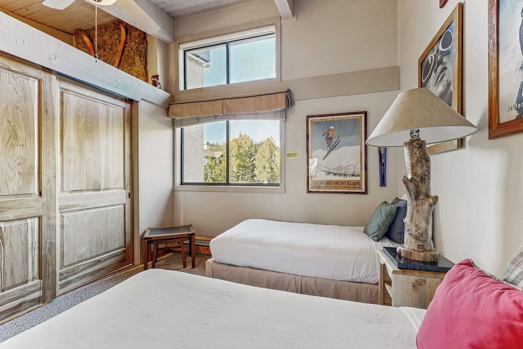 A bedroom with two beds, a window with a view, a lamp, and a framed picture on the wall.
