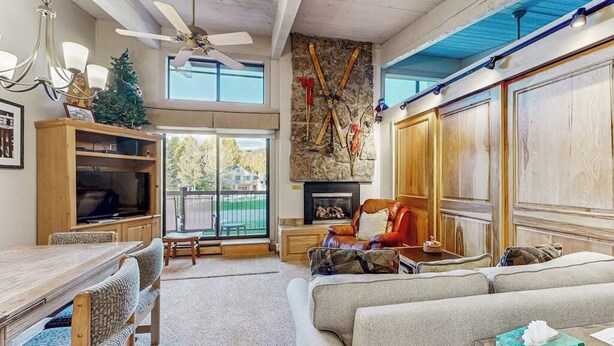 Un salon spacieux doté d’une cheminée, d’un ventilateur de plafond, d’une grande fenêtre et d’un mur en pierre.