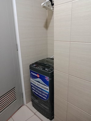 Ein Badezimmer mit weißen Fliesen, einer weißen Tür und einem schwarzen Warmwasserbereiter mit Fujidenso-Aufkleber.