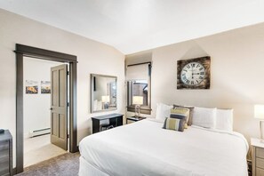 A hotel room with a bed, a desk, a chair, a clock, and a mirror. - Modern centrally located condo with pool, hot tub, gym & easy walk to lifts (Steamboat Springs)