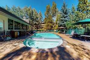 Ein Schwimmbecken mit Sonnendeck, umgeben von Bäumen und Gartenmöbeln.
