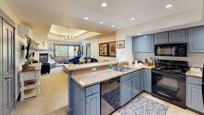 A modern kitchen with grey cabinets, a black stove, and a large island with a sink. - Canyon Creek B304 - Top-Floor Mountain Area Condo w/ Balcony, Gas Grill, Shared Heated Pool & Spa (Steamboat Springs)