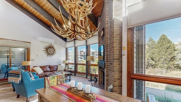 Amplia sala de estar con una gran mesa de madera, asientos cómodos, chimenea y ventanas amplias que ofrecen vistas al exterior.