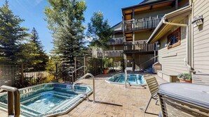 Un área de piscina con dos jacuzzis, una parrilla y un edificio con balcón.