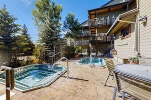 A pool area with two hot tubs, a barbecue, and a building with a balcony. - Beautiful mountain condo with balcony, deck, hot tub & pool & washer/dryer (Steamboat Springs)
