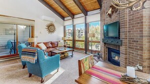 Amplia sala de estar con chimenea, televisor y un gran ventanal con vistas al exterior.