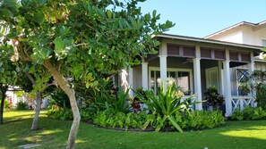 Ein Haus mit Veranda, umgeben von einem gepflegten Garten mit verschiedenen Pflanzen und einer Rasenfläche.
