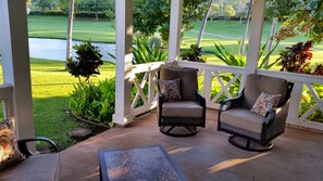 Eine überdachte Terrasse mit zwei Stühlen, einem kleinen Tisch und Blick auf einen Golfplatz.
